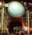 This cylindrical equipment with a large semispherical door is an autoclave, which layers film between two fabricated plates of glass, moves it into the cylindrical autoclave and applies high pressure for adhesion. The autoclave is 4 m in diameter.